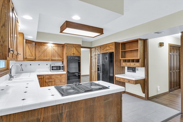 kitchen with sink, tile counters, black appliances, and kitchen peninsula