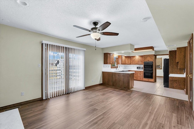 kitchen with a textured ceiling, light wood-type flooring, kitchen peninsula, ceiling fan, and black appliances