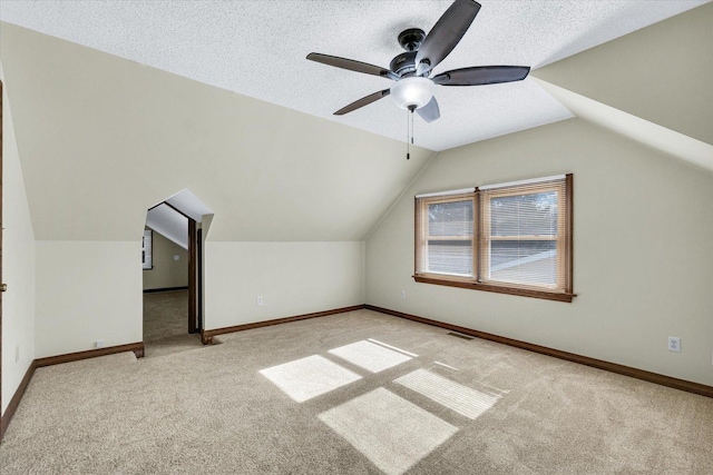 additional living space with vaulted ceiling, light colored carpet, ceiling fan, and a textured ceiling