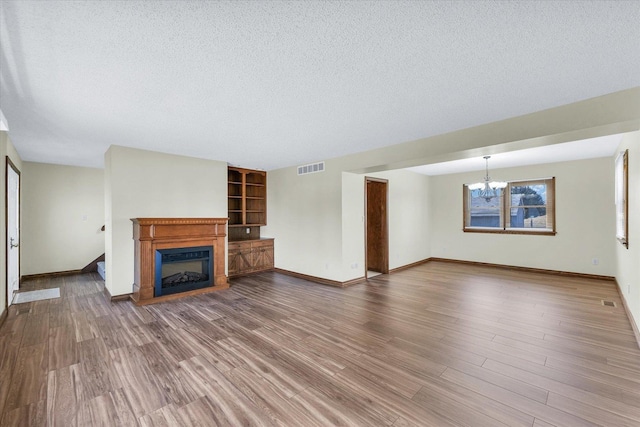 unfurnished living room with an inviting chandelier, wood-type flooring, and a textured ceiling