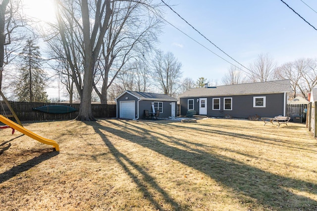 back of property with a lawn, an outdoor fire pit, a playground, a garage, and an outdoor structure