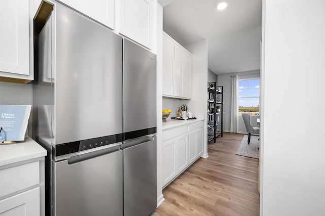 kitchen with light stone countertops, light wood-type flooring, white cabinets, and stainless steel refrigerator