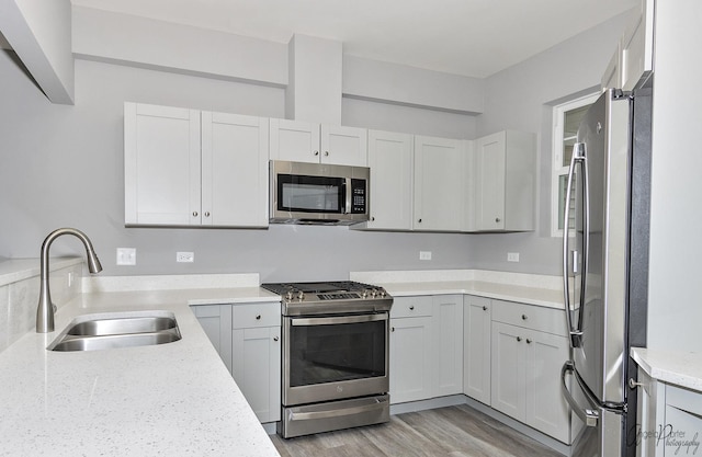 kitchen featuring appliances with stainless steel finishes, sink, white cabinets, light stone countertops, and light hardwood / wood-style flooring