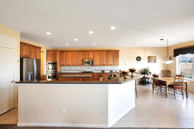 kitchen featuring hanging light fixtures, backsplash, stainless steel appliances, and a center island with sink