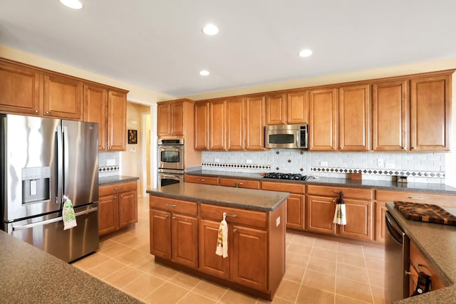 kitchen with light tile patterned flooring, appliances with stainless steel finishes, a kitchen island, and backsplash