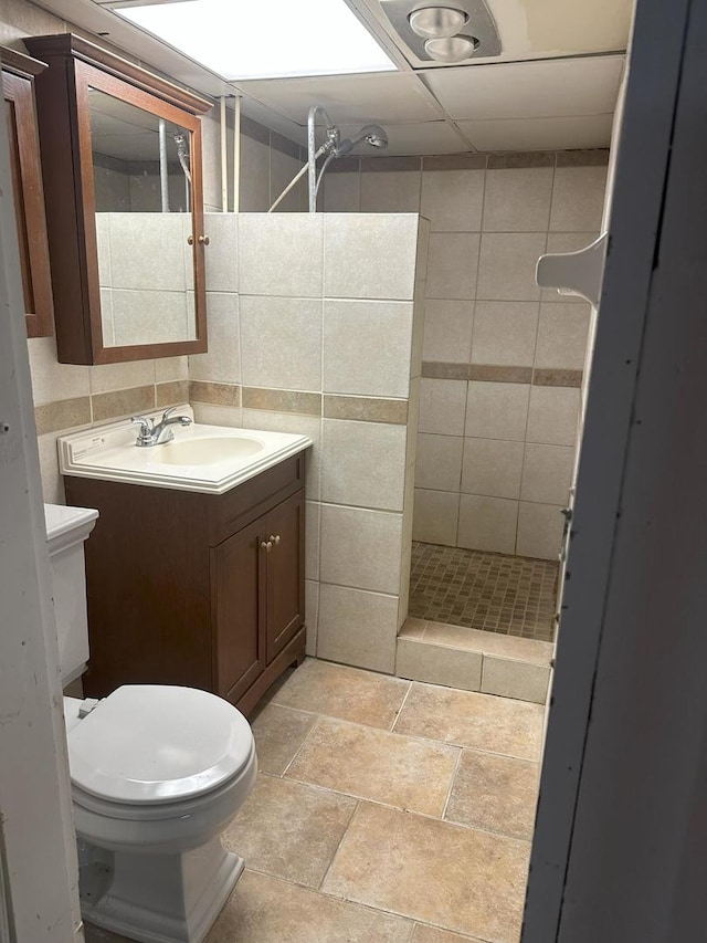 bathroom featuring tile walls, tiled shower, vanity, decorative backsplash, and toilet