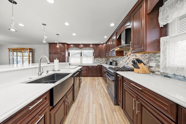 kitchen with pendant lighting, sink, wall chimney range hood, stainless steel appliances, and decorative backsplash