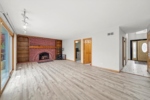 unfurnished living room with plenty of natural light, a brick fireplace, built in features, and light hardwood / wood-style flooring