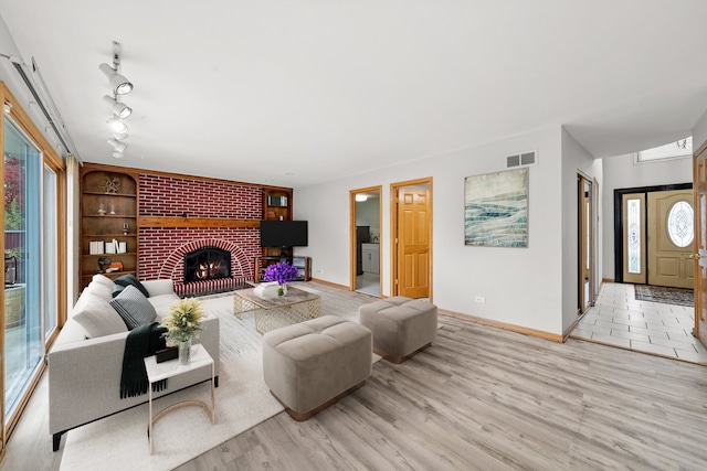 living room with a fireplace, light hardwood / wood-style flooring, built in features, and rail lighting