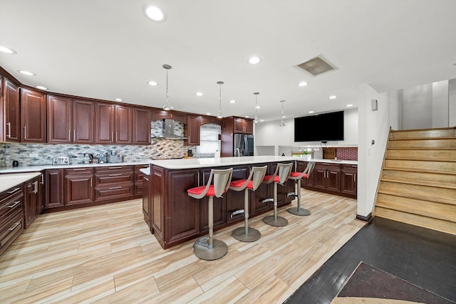 kitchen with wall chimney range hood, a breakfast bar area, hanging light fixtures, stainless steel refrigerator with ice dispenser, and a kitchen island