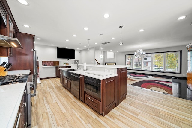 kitchen with a large island, sink, hanging light fixtures, stainless steel appliances, and light wood-type flooring