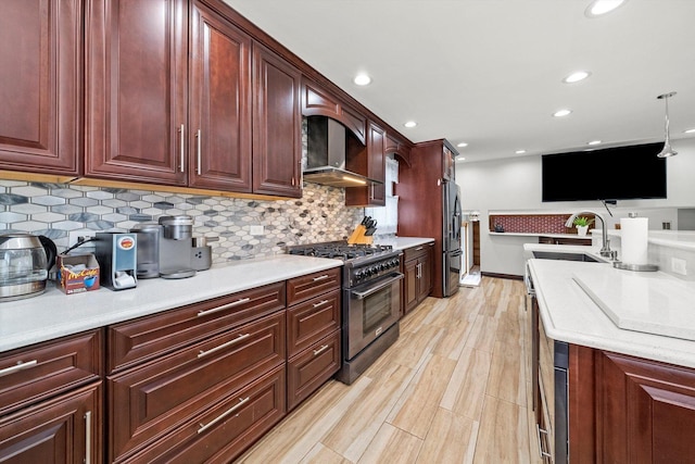 kitchen with pendant lighting, appliances with stainless steel finishes, decorative backsplash, wall chimney exhaust hood, and light wood-type flooring