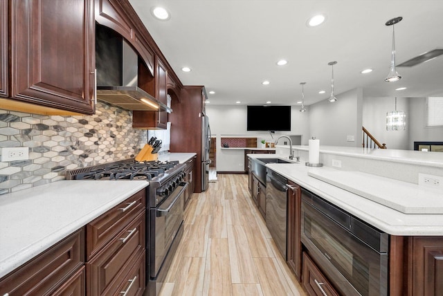 kitchen featuring pendant lighting, sink, stainless steel appliances, light wood-type flooring, and wall chimney exhaust hood