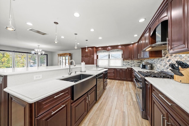 kitchen featuring sink, tasteful backsplash, decorative light fixtures, a center island with sink, and high end stainless steel range oven