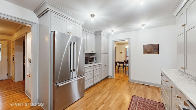 kitchen with light stone countertops, white cabinets, light hardwood / wood-style floors, crown molding, and high end refrigerator