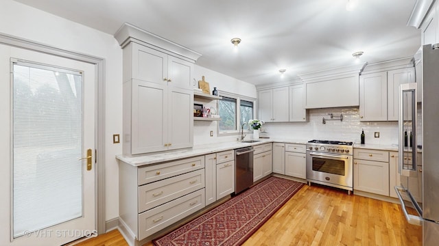 kitchen featuring light stone counters, premium appliances, decorative backsplash, light hardwood / wood-style floors, and sink