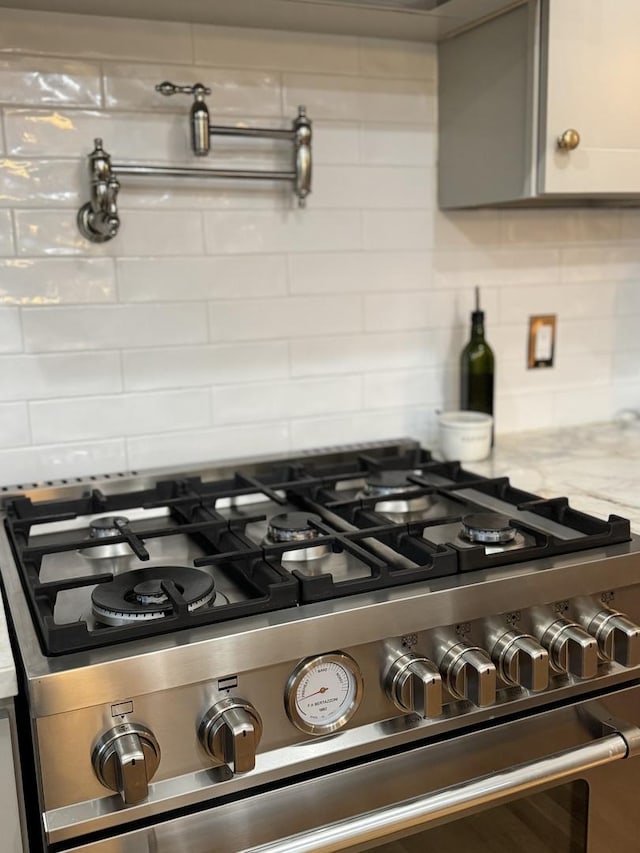 room details with gray cabinetry, stainless steel range with gas stovetop, light stone counters, and backsplash