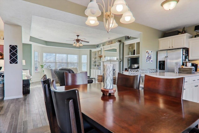 dining area with hardwood / wood-style floors, ceiling fan with notable chandelier, and built in shelves