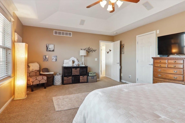 bedroom with ceiling fan, light colored carpet, and a raised ceiling