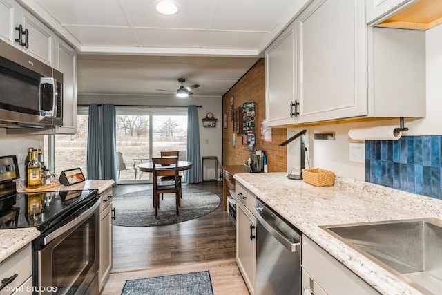 kitchen featuring sink, ceiling fan, stainless steel appliances, light stone countertops, and light wood-type flooring