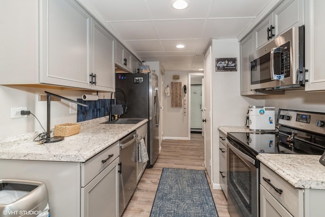 kitchen with a paneled ceiling, appliances with stainless steel finishes, light wood-type flooring, and gray cabinetry