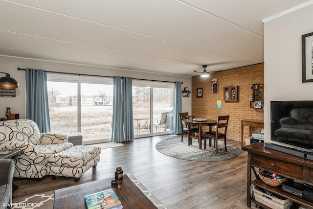 living room with hardwood / wood-style flooring, ceiling fan, brick wall, and crown molding