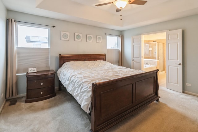 bedroom featuring ceiling fan, connected bathroom, a tray ceiling, and light carpet