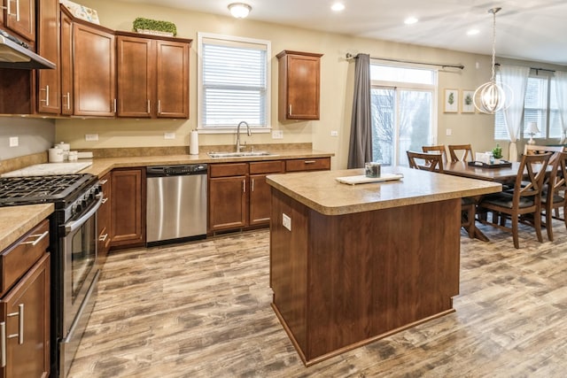 kitchen with sink, appliances with stainless steel finishes, light hardwood / wood-style floors, a kitchen island, and decorative light fixtures