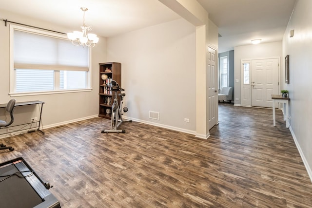 workout area featuring dark hardwood / wood-style flooring, a healthy amount of sunlight, and an inviting chandelier