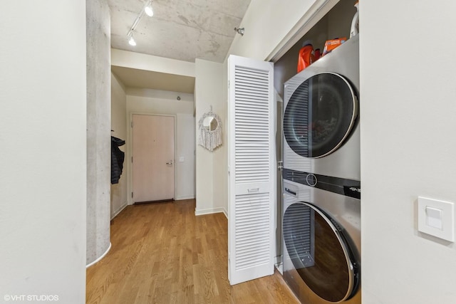 washroom featuring stacked washing maching and dryer, track lighting, and light hardwood / wood-style floors