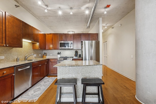 kitchen featuring sink, stainless steel appliances, a center island, light stone counters, and wood-type flooring