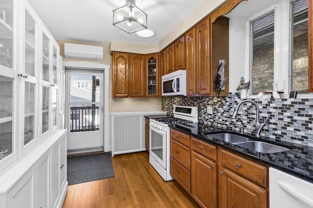 kitchen with an AC wall unit, sink, dark stone countertops, light hardwood / wood-style floors, and white appliances