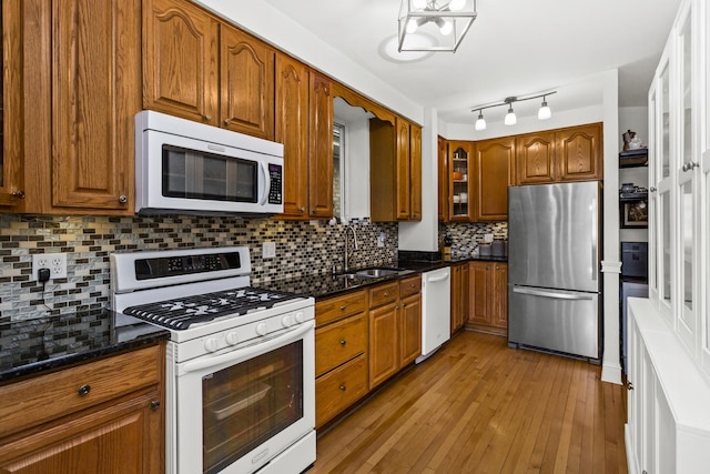 kitchen featuring sink, light hardwood / wood-style flooring, dark stone countertops, white appliances, and decorative backsplash