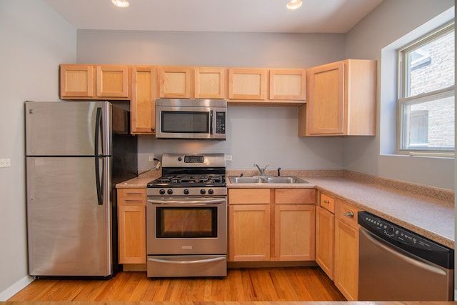 kitchen featuring stainless steel appliances, sink, light brown cabinets, and light wood-type flooring