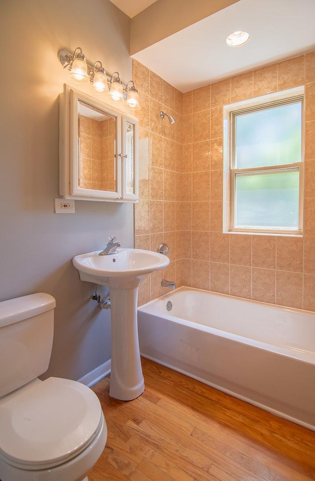 bathroom featuring hardwood / wood-style flooring, tiled shower / bath, and toilet