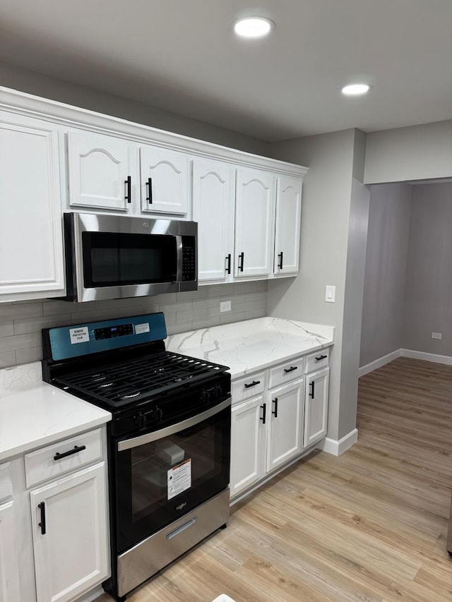 kitchen with light stone counters, light hardwood / wood-style flooring, stainless steel appliances, decorative backsplash, and white cabinets