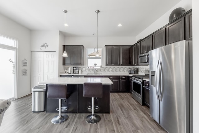 kitchen featuring dark brown cabinetry, appliances with stainless steel finishes, hanging light fixtures, and a kitchen island