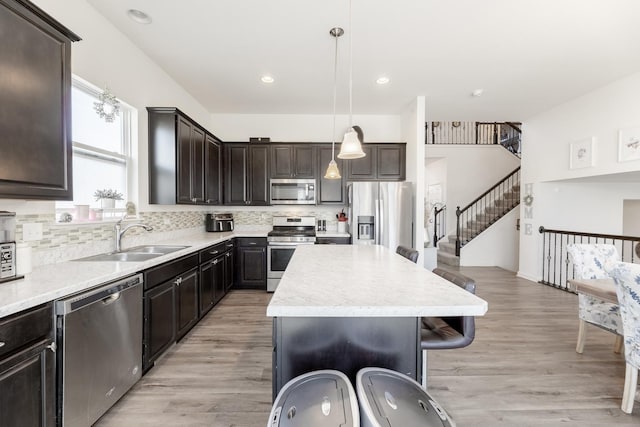 kitchen with a kitchen island, appliances with stainless steel finishes, sink, hanging light fixtures, and light wood-type flooring