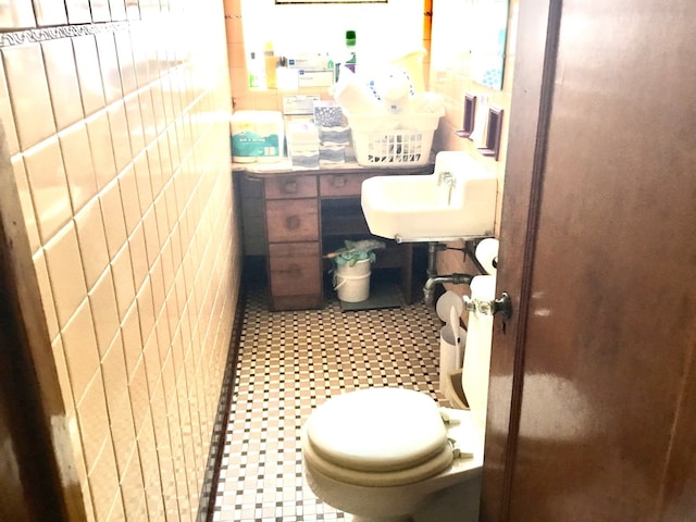 bathroom with toilet, sink, and tile walls