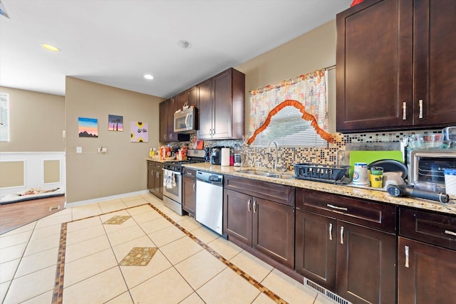 kitchen with light tile patterned flooring, sink, light stone counters, stainless steel appliances, and backsplash