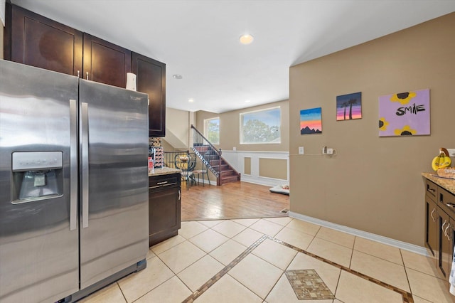 kitchen featuring dark brown cabinetry, stainless steel fridge with ice dispenser, light stone counters, and light tile patterned flooring