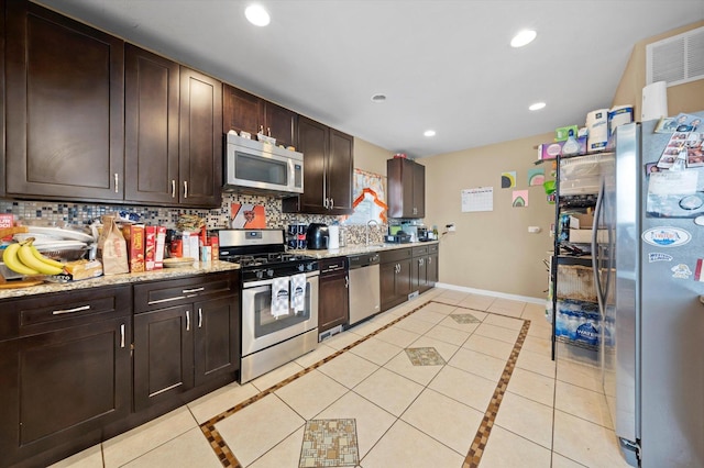 kitchen with backsplash, stainless steel appliances, dark brown cabinetry, light stone counters, and light tile patterned flooring