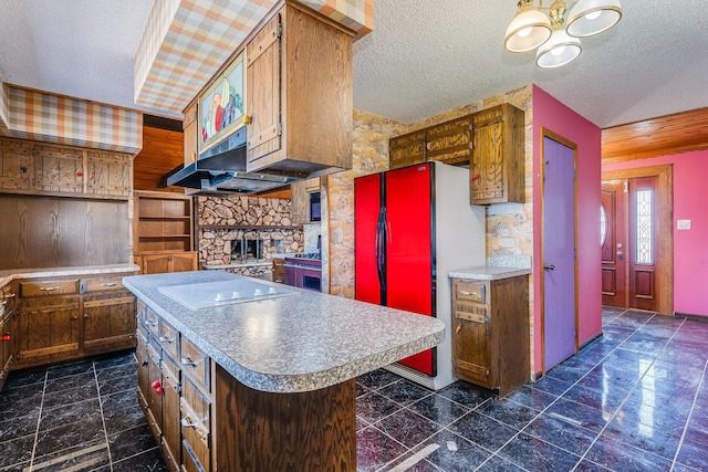 kitchen featuring a kitchen island, a fireplace, refrigerator, electric cooktop, and a textured ceiling