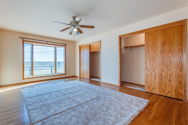 unfurnished bedroom featuring multiple closets, hardwood / wood-style flooring, and ceiling fan