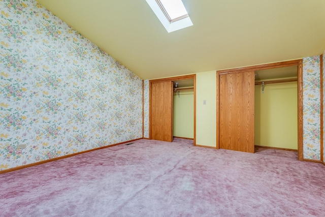 unfurnished bedroom with light carpet, lofted ceiling with skylight, and multiple closets