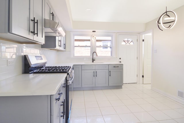 kitchen featuring gray cabinets, stainless steel gas stove, sink, decorative backsplash, and hanging light fixtures