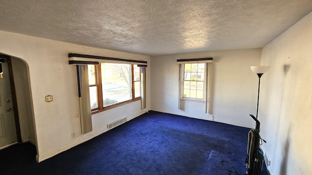 spare room featuring a textured ceiling and dark colored carpet