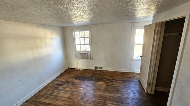 empty room featuring cooling unit, a textured ceiling, and dark hardwood / wood-style flooring