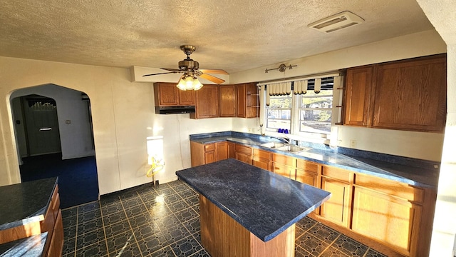 kitchen with a kitchen island, sink, a textured ceiling, and ceiling fan