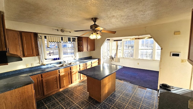 kitchen featuring ceiling fan, a kitchen island, sink, and a textured ceiling